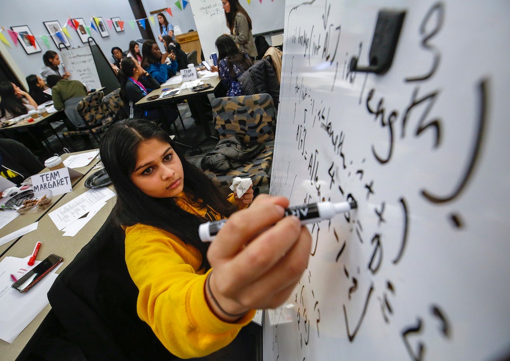 A student works on a solution on a white board in a classroom.