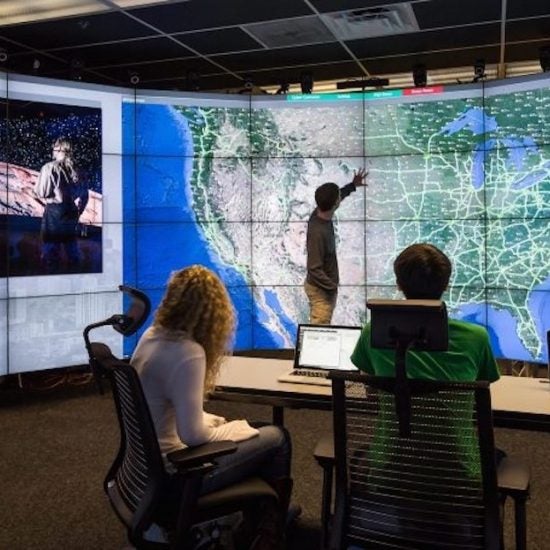 A group of students work in the EVL lab looking at a map of the United States on the lab's screens