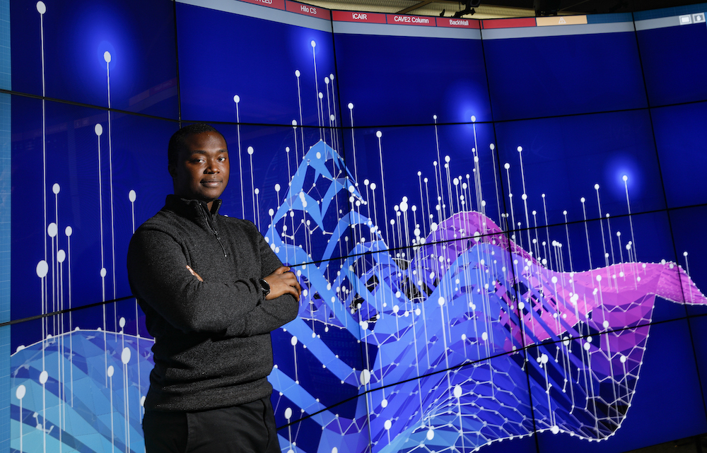 A UIC data science student with a blue, purple, and pink data visualization in UIC's Electronic Visualization Lab