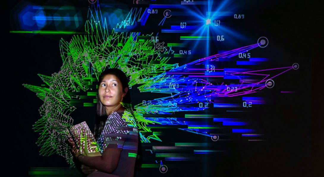 Michelle posed on a black background amid a colorful green and blue projection of visualized data